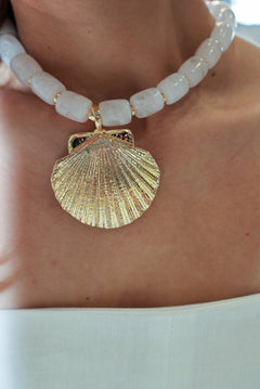Close-up of a gold shell pendant on a white beaded necklace.