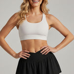 Woman wearing a white sports bra and black skirt against a clear blue sky.