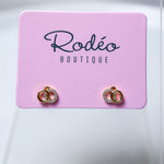 A pair of tiny gold hoop earrings with clear rhinestone small hoop, displayed on a pink card labeled 'Rodéo BOUTIQUE' against a light gray background.