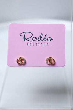 A pair of tiny gold hoop earrings with clear rhinestone small hoop, displayed on a pink card labeled 'Rodéo BOUTIQUE' against a light gray background.