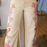 White jeans with colorful floral embroidery on a wooden floor.