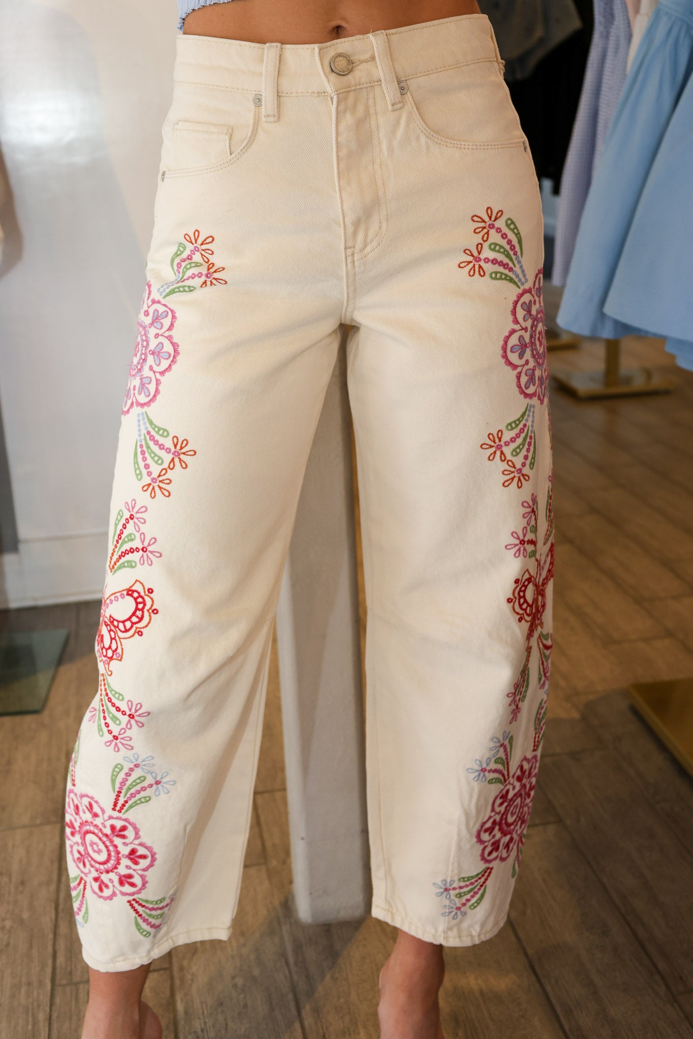 White jeans with colorful floral embroidery on a wooden floor.