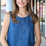 Woman wearing a denim sleeveless top standing outdoors.