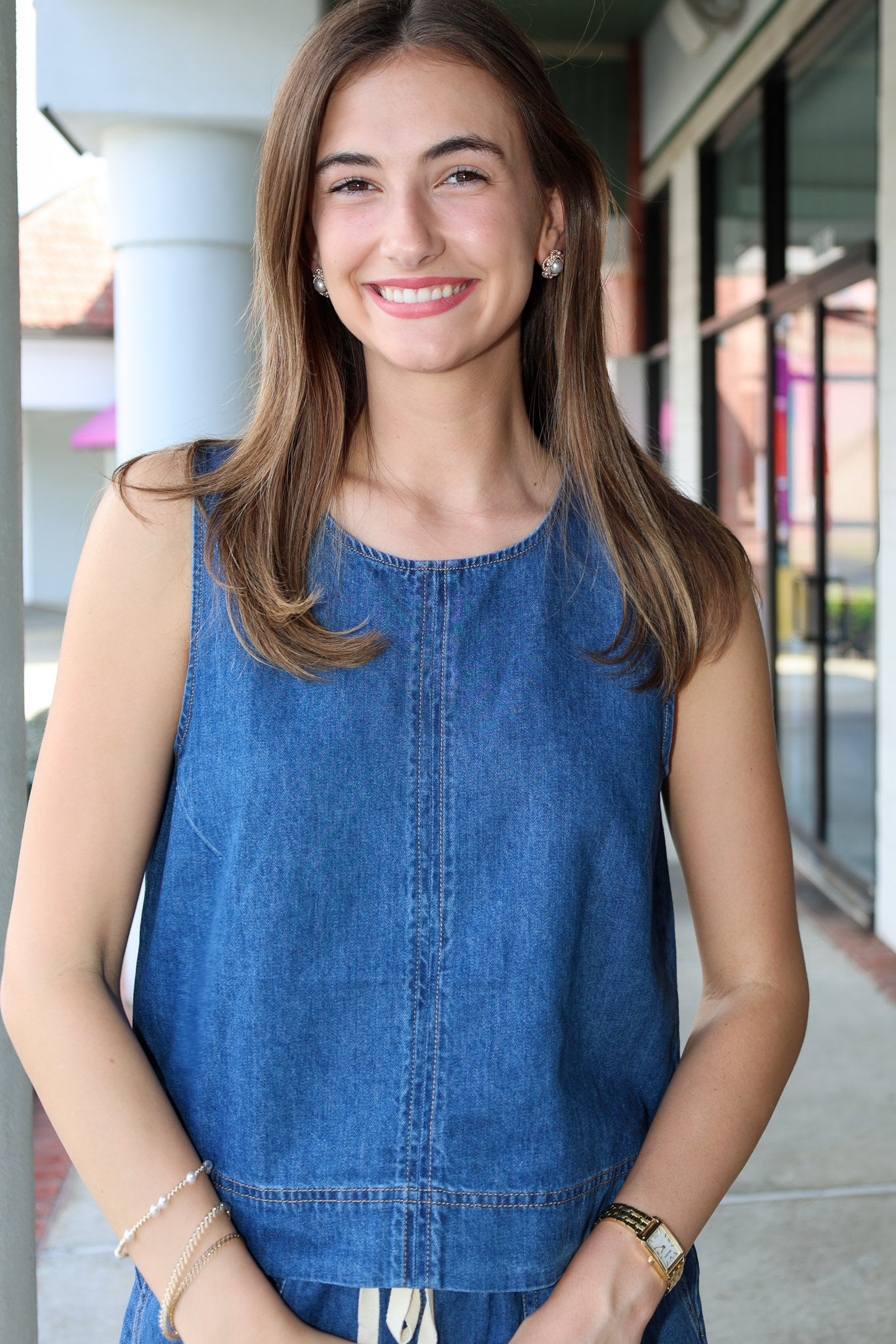 Woman wearing a denim sleeveless top standing outdoors.