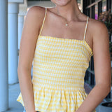 Woman wearing a yellow checkered top and denim shorts outdoors.
