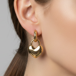 Gold heart-shaped padlock style earring worn by a person with a neutral background
