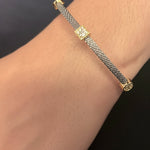 A close-up of a person's wrist wearing a delicate silver-toned chain bracelet with small gold-toned decorative links, paired with a frayed denim cuff.