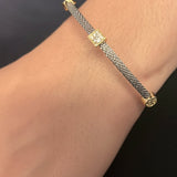 A close-up of a person's wrist wearing a delicate silver-toned chain bracelet with small gold-toned decorative links, paired with a frayed denim cuff.