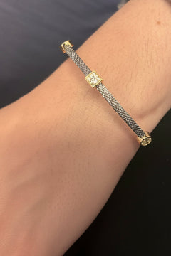 A close-up of a person's wrist wearing a delicate silver-toned chain bracelet with small gold-toned decorative links, paired with a frayed denim cuff.