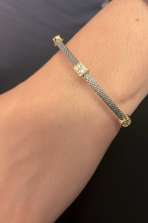 A close-up of a person's wrist wearing a delicate silver-toned chain bracelet with small gold-toned decorative links, paired with a frayed denim cuff.