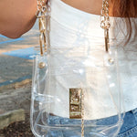 Person wearing a clear handbag with gold chain strap outdoors