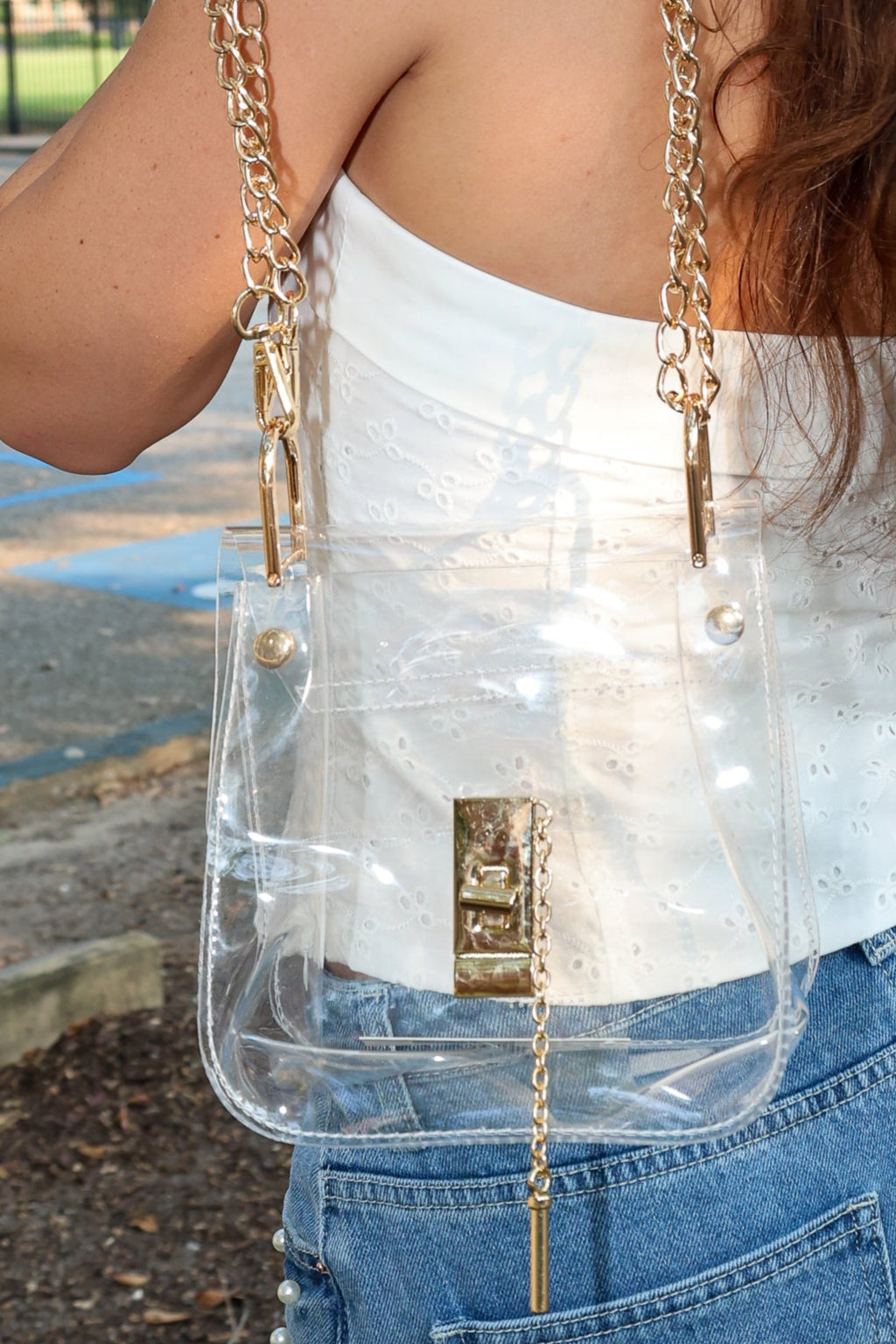 Person wearing a clear handbag with gold chain strap outdoors