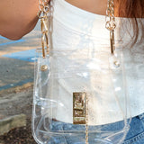 Person wearing a clear handbag with gold chain strap outdoors