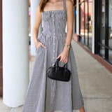 Woman wearing a black and white checkered dress holding a black handbag on a sidewalk.