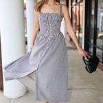 Woman in a checkered dress standing outdoors near columns.