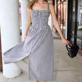 Woman in a checkered dress standing outdoors near columns.