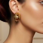 A pair of gold hoop earrings with three brown tiger's eye stones each, displayed on a pink Rodéo Boutique card.