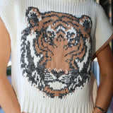 A close-up of a woman wearing a cream ribbed knit sweater with a large knitted tiger face graphic on the front in beige, brown, and black.