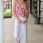 Woman wearing a floral top and white pants standing on a sidewalk.