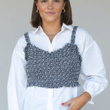 Woman wearing a white shirt with a black and gray patterned top over it against a plain background