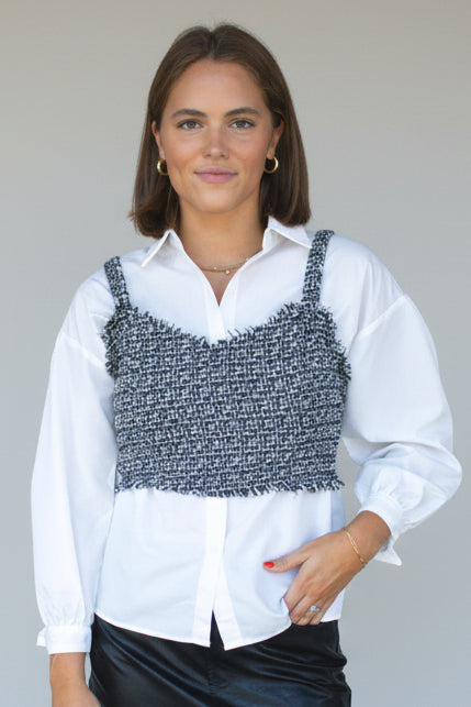 Woman wearing a white shirt with a black and gray patterned top over it against a plain background