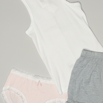 Collection of women's clothing including a white tank top, gray shorts, lace panties, and socks on a pink background.