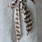 White cowboy boots with a decorative tiger print ribbon on a neutral background