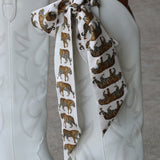 White cowboy boots with a decorative tiger print ribbon on a neutral background