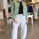Woman in a green jacket and white pants standing in a store.