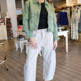 Woman in a green jacket and white pants standing in a store.