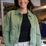 Woman wearing a green denim cropped jacket and black top in an indoor setting