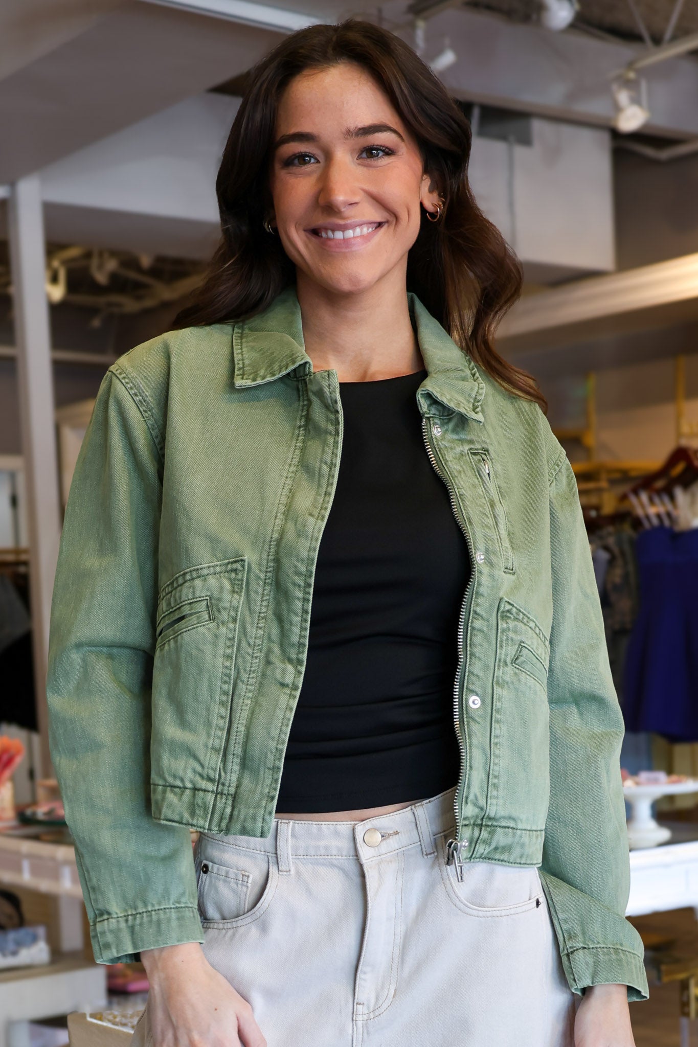 Woman wearing a green denim cropped jacket and black top in an indoor setting