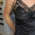 A woman wearing a black satin camisole top with black lace trim and tie details on the straps, photographed at Rodeo boutique .