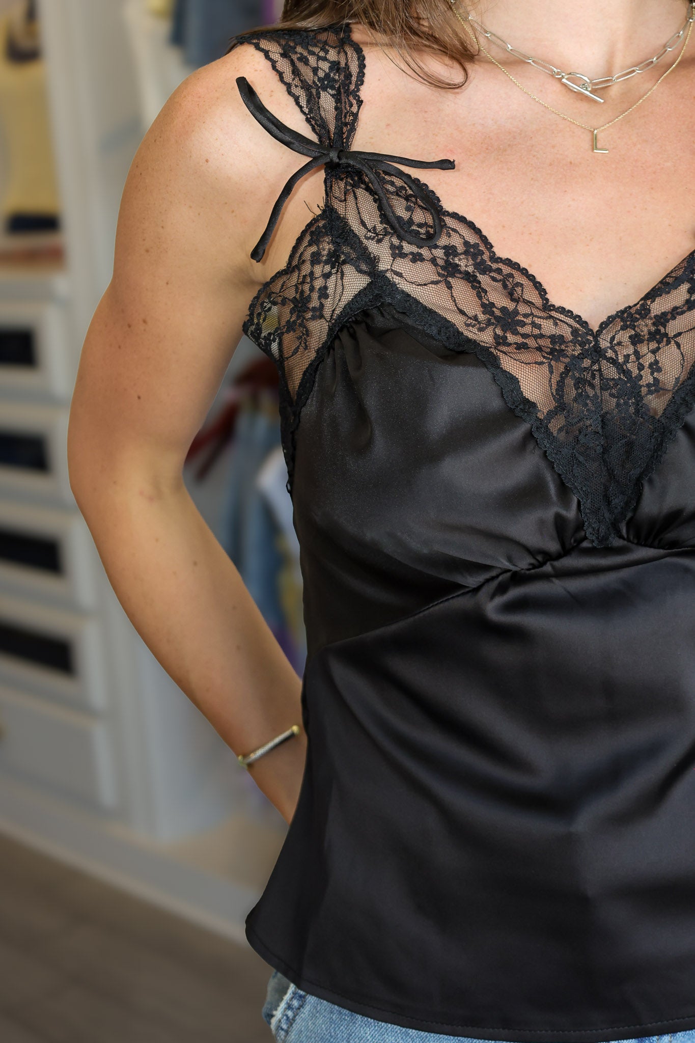 A woman wearing a black satin camisole top with black lace trim and tie details on the straps, photographed at Rodeo boutique .