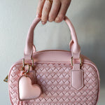 Pink woven handbag with a heart-shaped keychain held by a hand against a light background