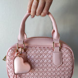 Pink woven handbag with a heart-shaped keychain held by a hand against a light background