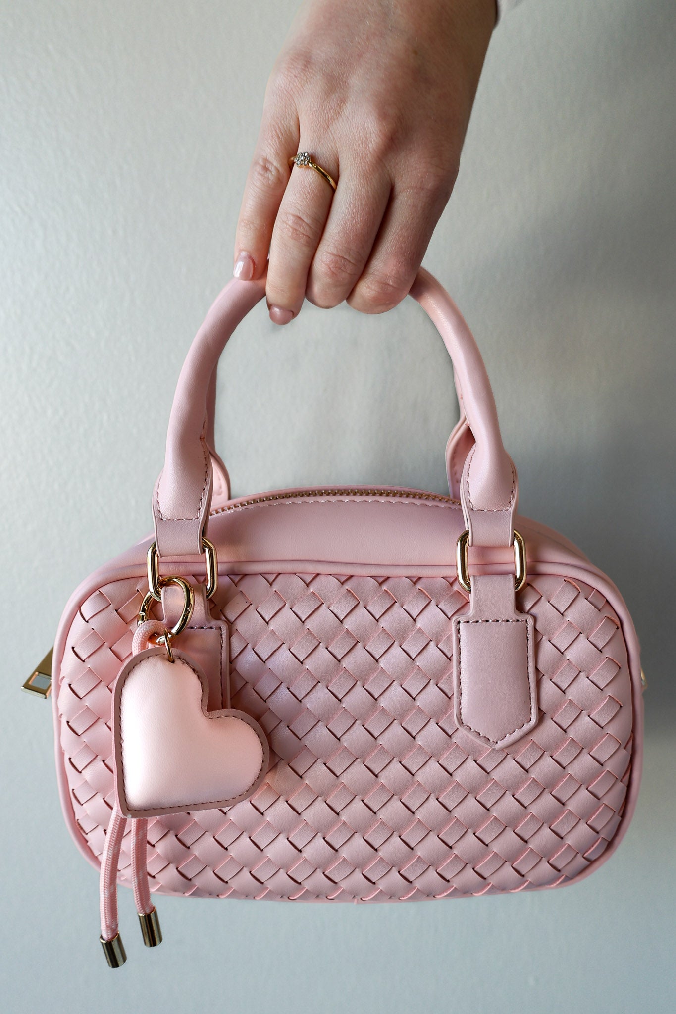Pink woven handbag with a heart-shaped keychain held by a hand against a light background