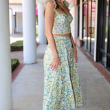 Woman in a floral skirt set standing on a sidewalk with columns in the background