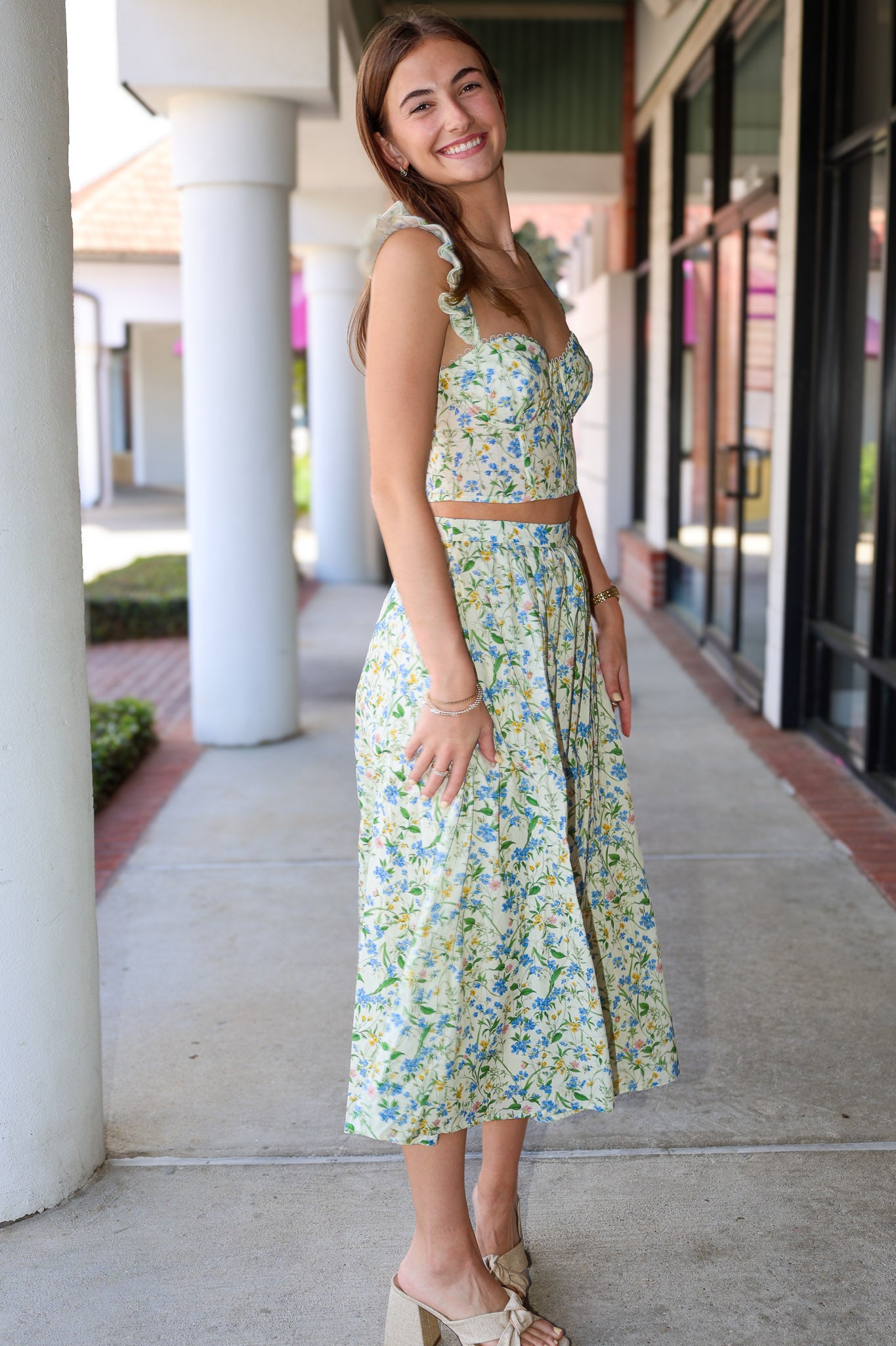 Woman in a floral skirt set standing on a sidewalk with columns in the background