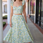 Woman wearing a green floral skirt set standing outdoors on a sidewalk.