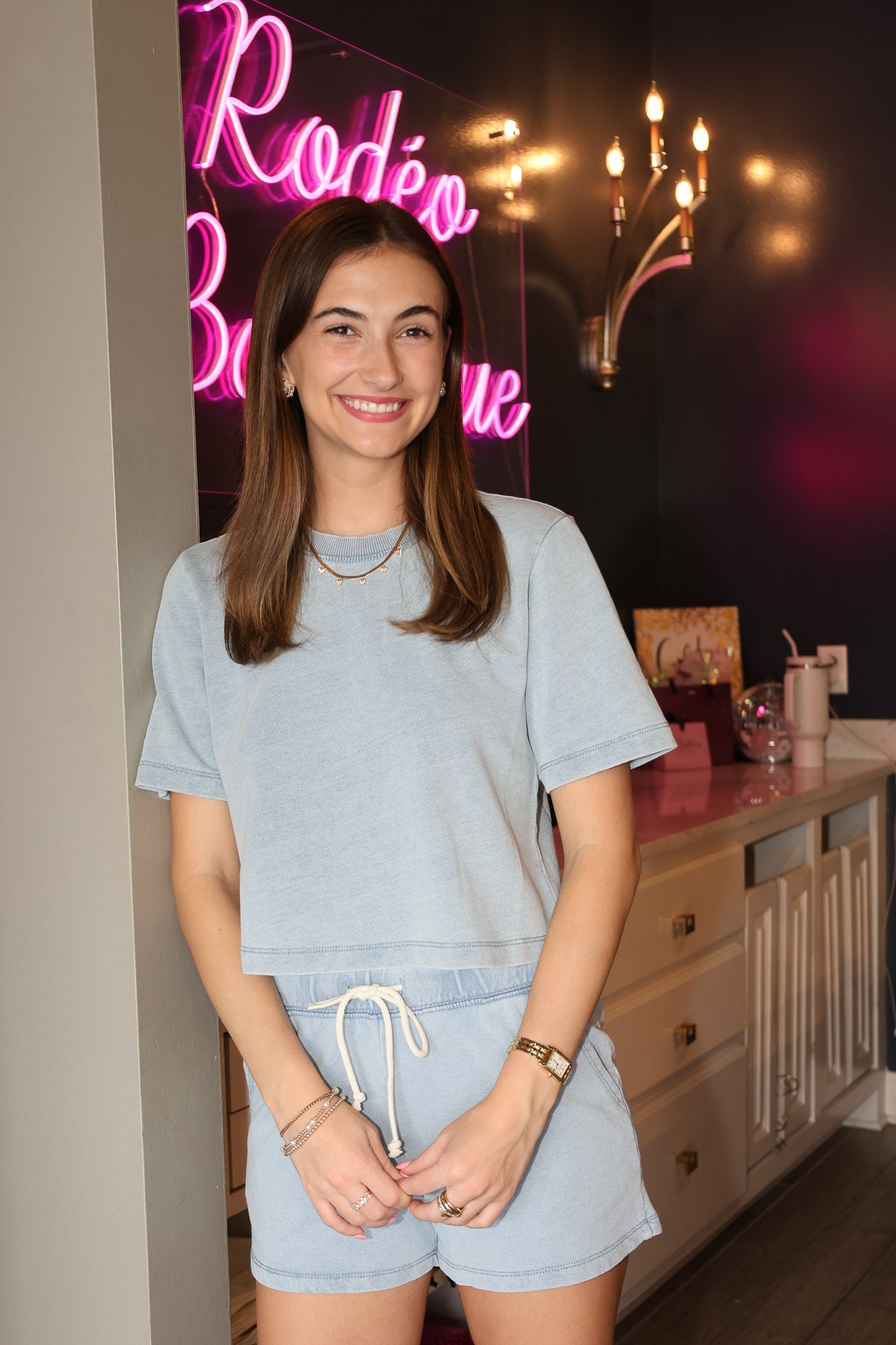 Woman in light blue outfit standing in front of a neon sign indoors