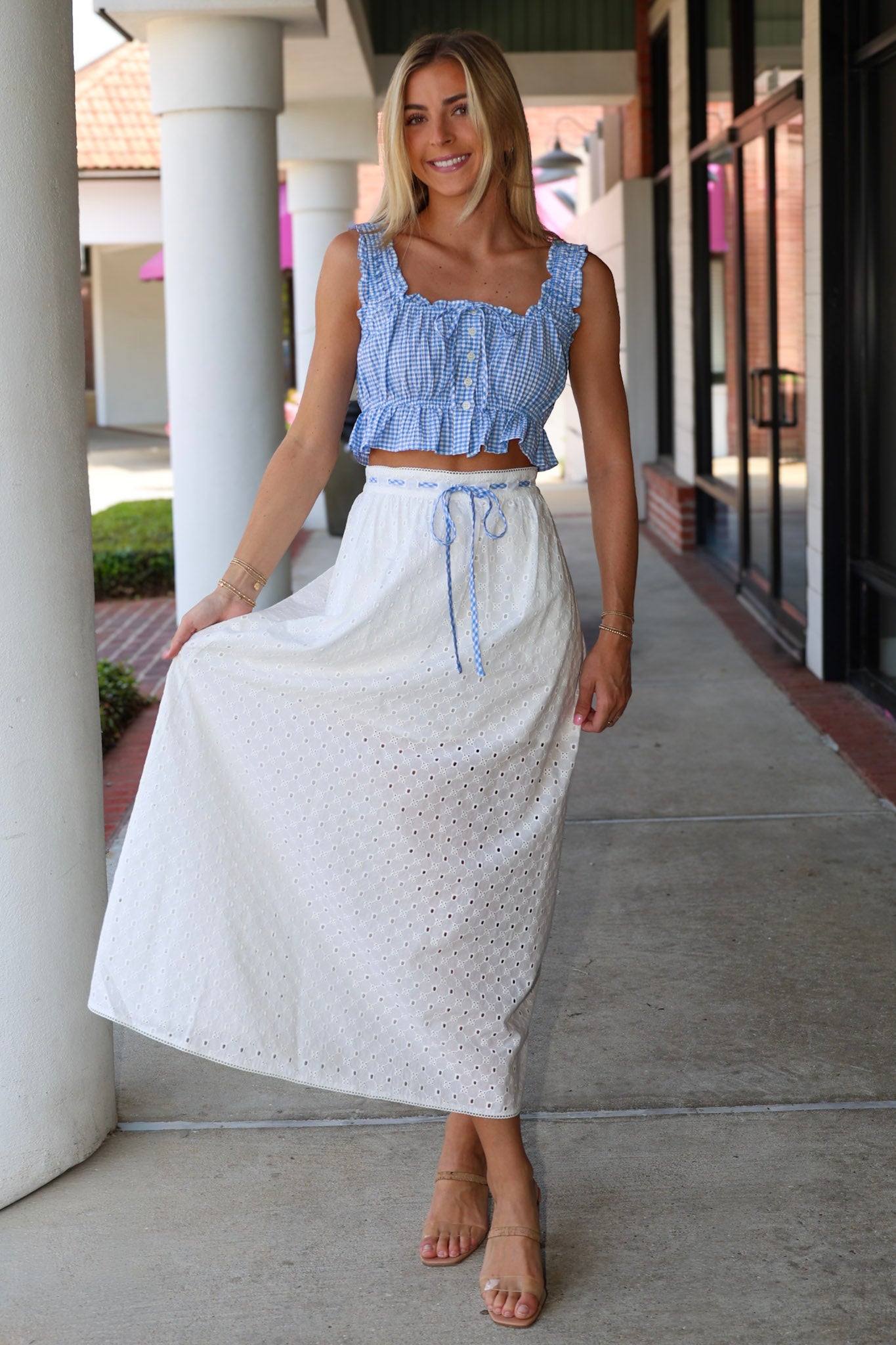 Woman wearing a blue top and white skirt standing on a sidewalk.